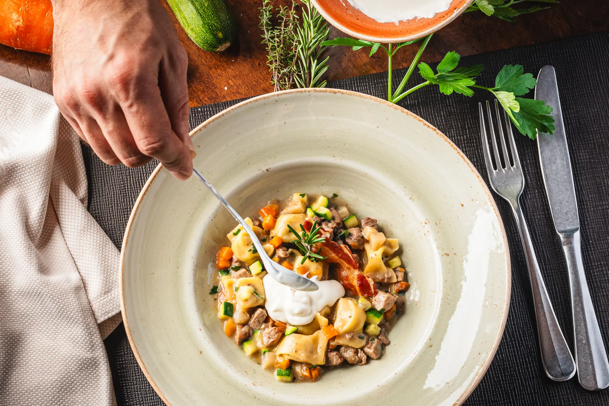 {"sl":"Oseba dodaja smetano na kro\u017enik z ravioli, zelenjavo in mesom, pripravljeno za serviranje z vilico in no\u017eem na strani.","en":"","de":"","it":""}