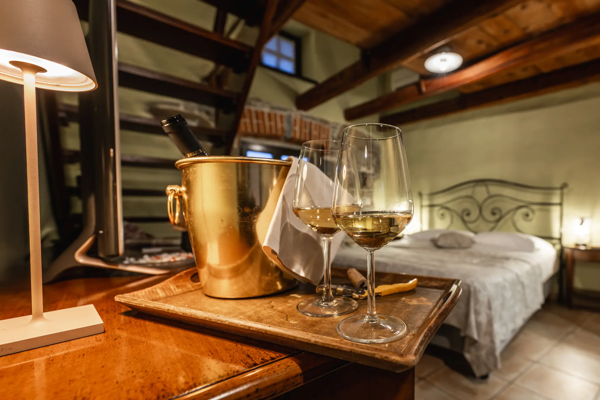 {"sl":"Dve kozarci belega vina na pladnju poleg vedra s steklenico v romanti\u010dno urejeni spalnici z lesenimi tramovi in posteljo v ozadju.","en":"","de":"","it":""}