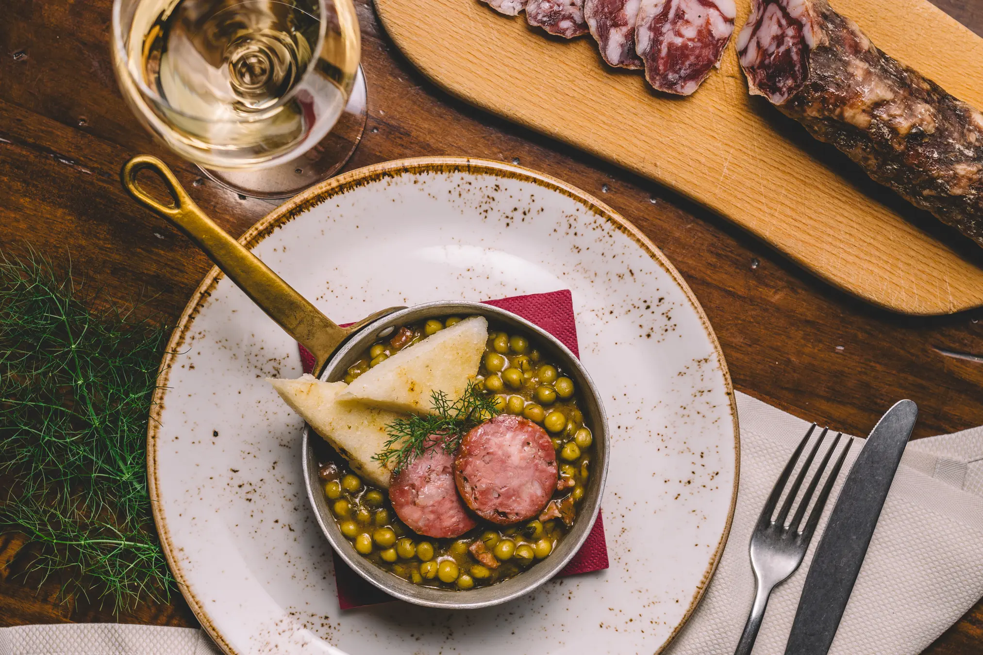 {"sl":"Posoda z jedjo iz graha, klobase in kruha, ob kozarec vina in narezan mesni izdelek na rezalni deski.","en":"","de":"","it":""}